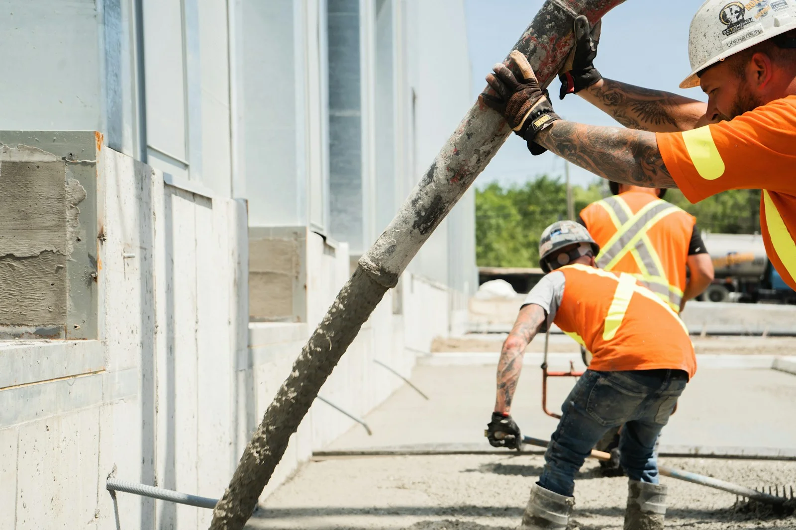 Concrete crew guiding a pump hose and finishing a fresh slab on an active construction site